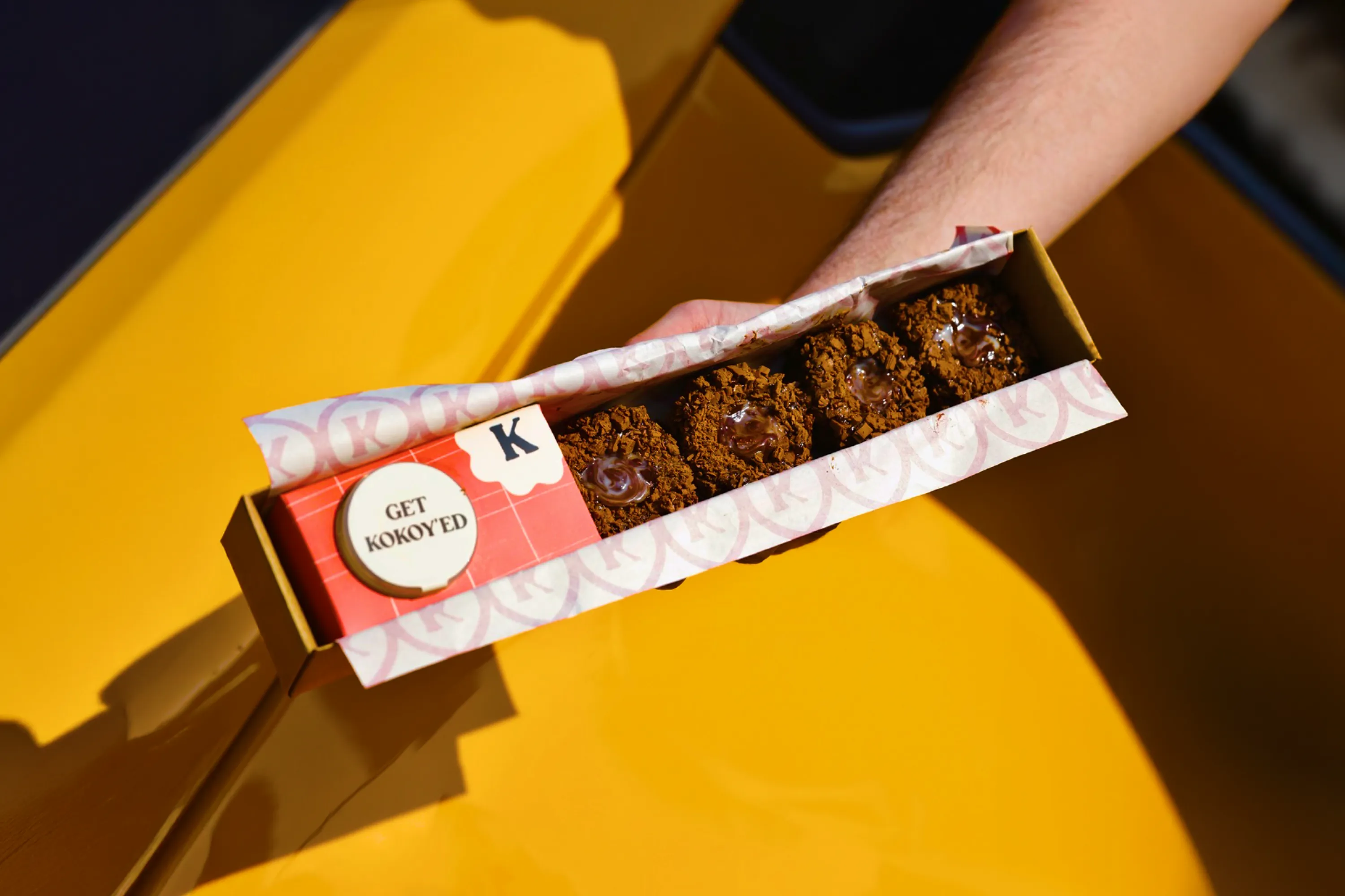 Kokoy chocolate dessert box held above a yellow car.