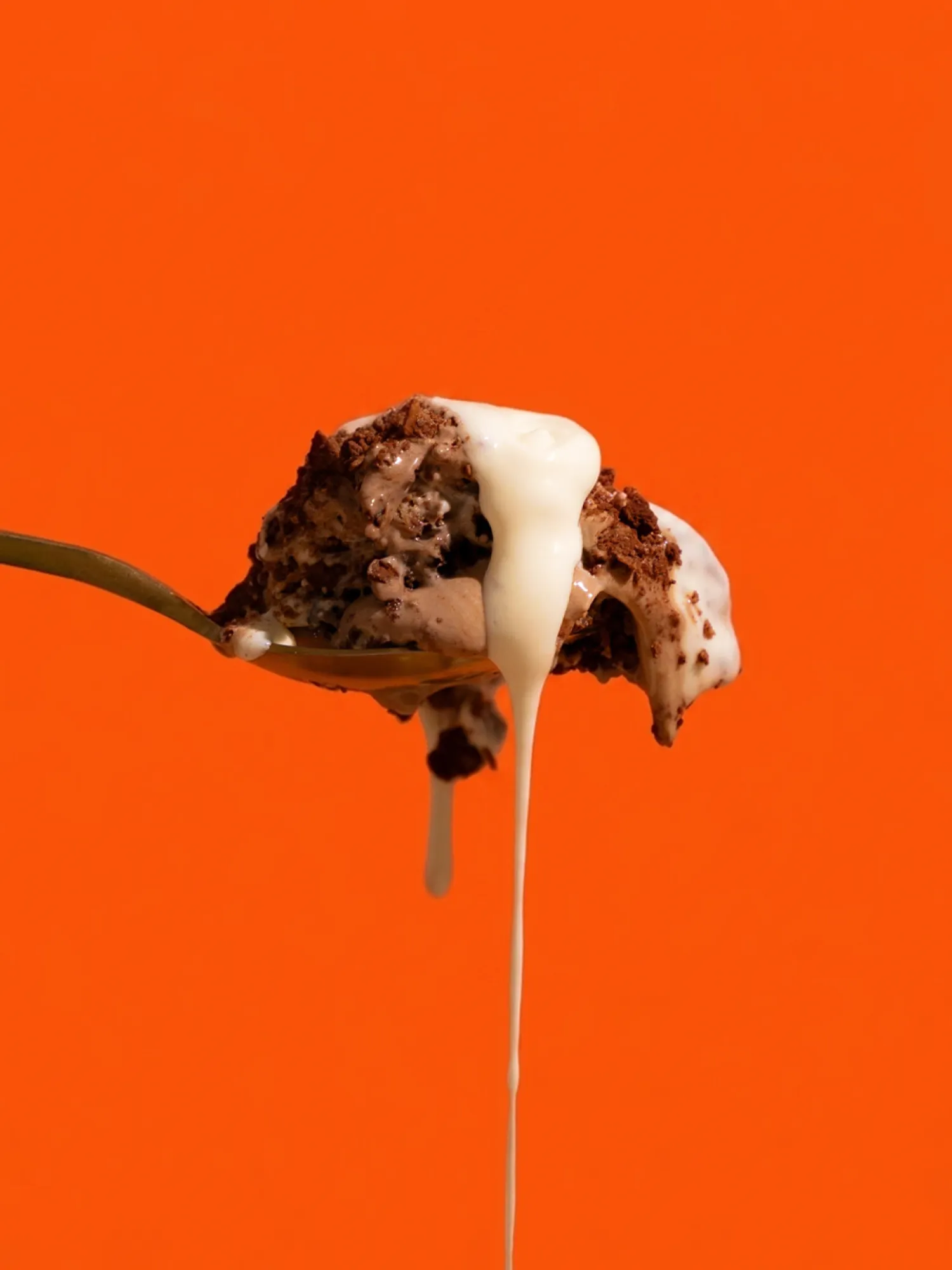 A spoonful of chocolate dessert with cream against orange.